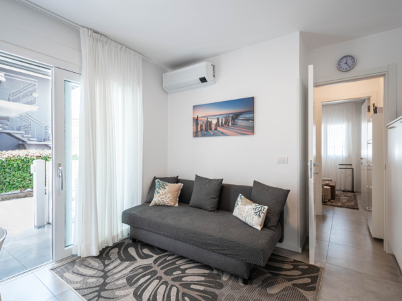 Soggiorno con divano e accesso al patio del bilocale a Lignano Sabbiadoro, a circa 150 metri dal mare